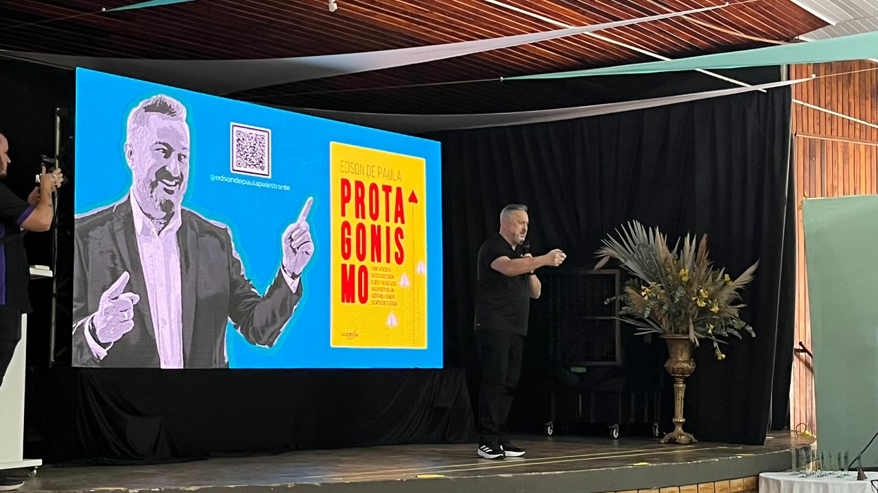 Palestrante Edson de Paula em apresentação sobre protagonismo, ao lado de telão com arte gráfica do seu livro.