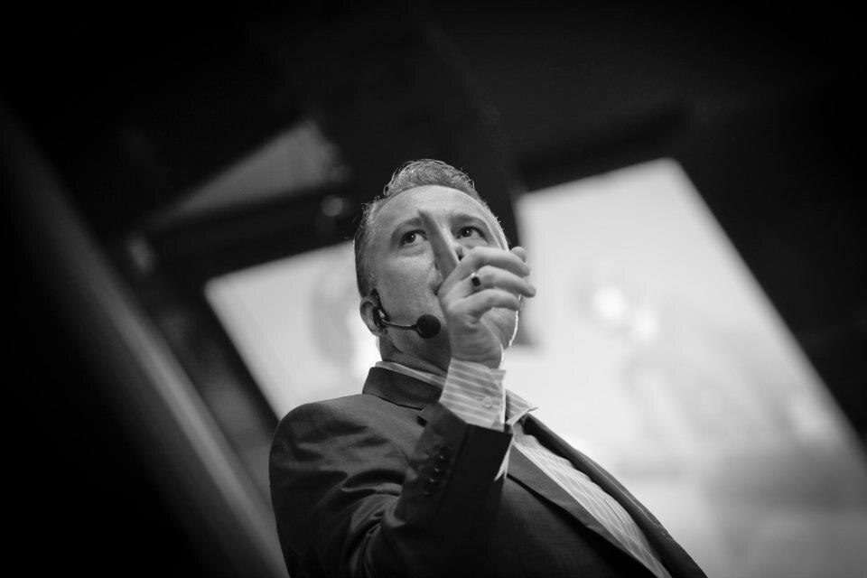 Palestrante Edson de Paula em apresentação, usando microfone auricular e fazendo gesto enfático com a mão.