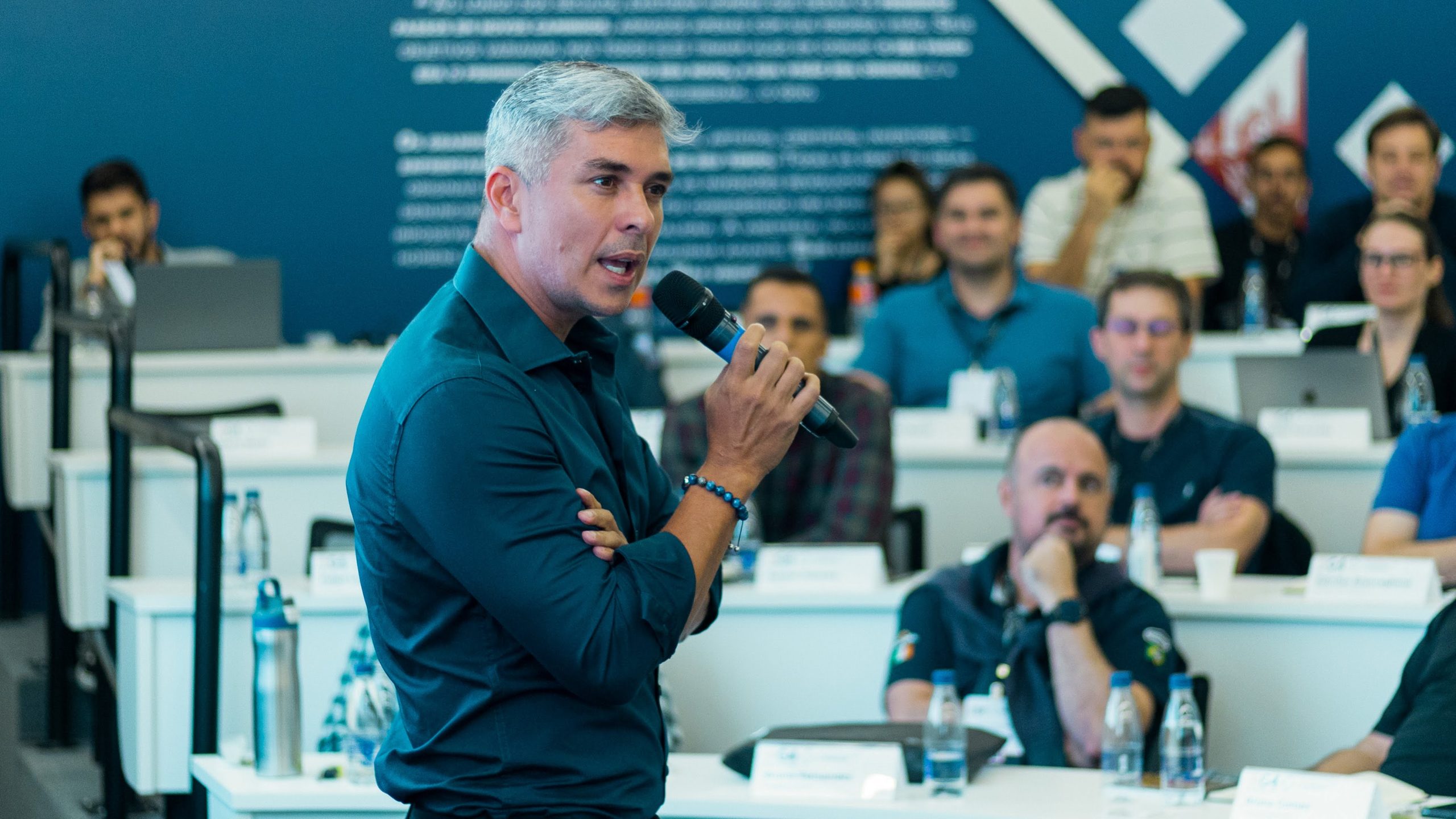 Ivan Moré segurando um microfone enquanto palestra para uma plateia corporativa atenta, representando a força de quebrar padrões no trabalho com propósito.